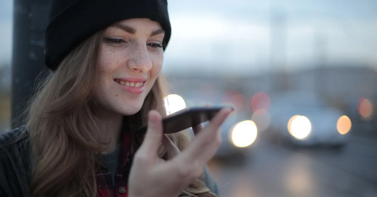 Jeune femme souriante utilisant un smartphone dans une rue urbaine pendant le crépuscule.