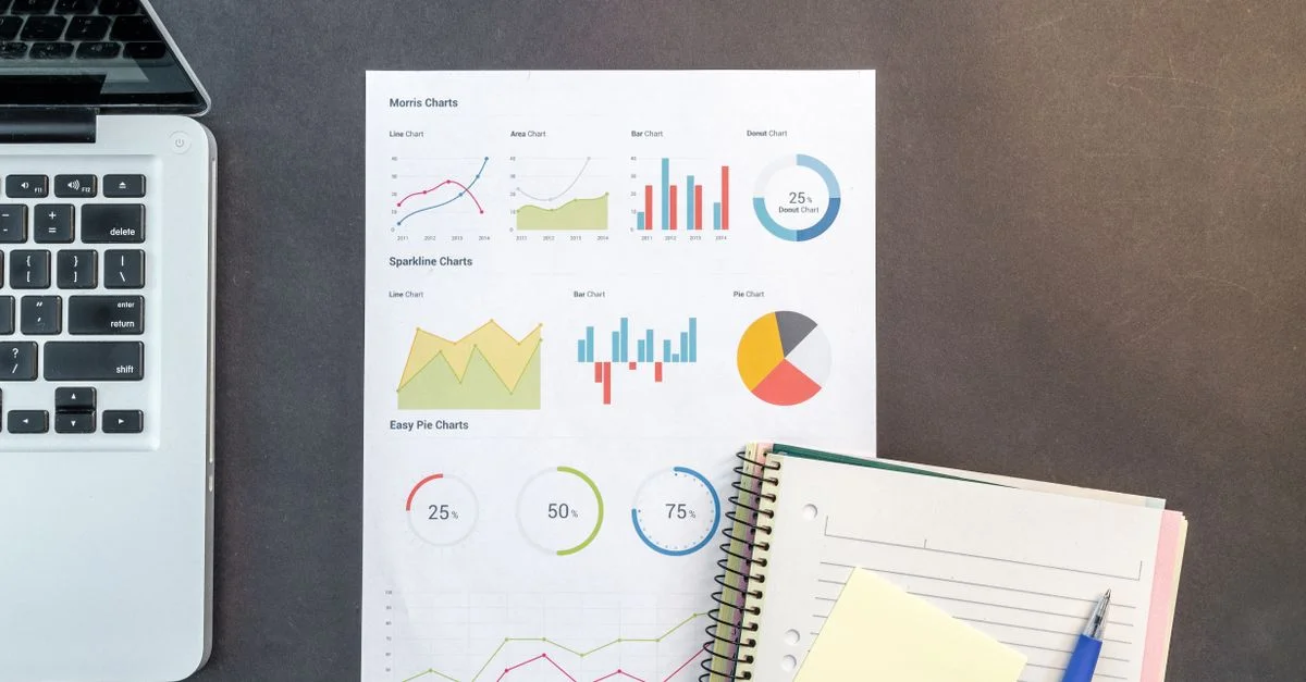 Vue de dessus d'un bureau avec des graphiques, un ordinateur portable et des carnets, idéal pour des thèmes d'analyse de données.
