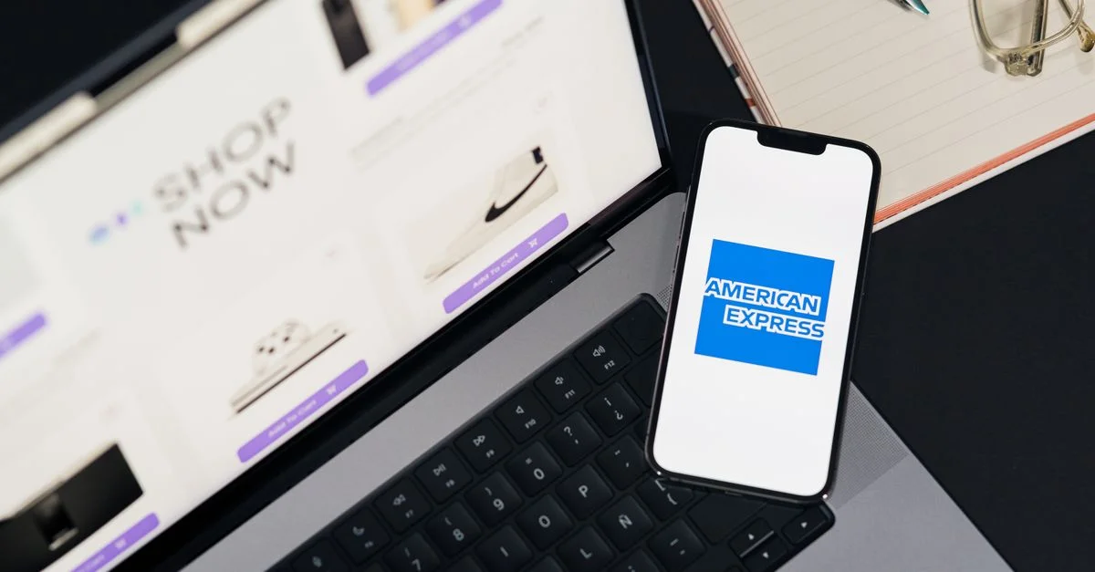 Smartphone affichant le logo American Express sur un ordinateur portable pour faciliter les achats en ligne.
