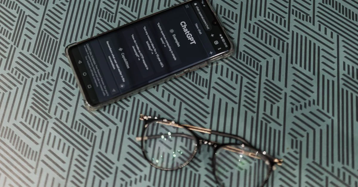 Gros plan sur un smartphone affichant ChatGPT à côté de lunettes sur une surface à motifs mettant en valeur la technologie et le style.