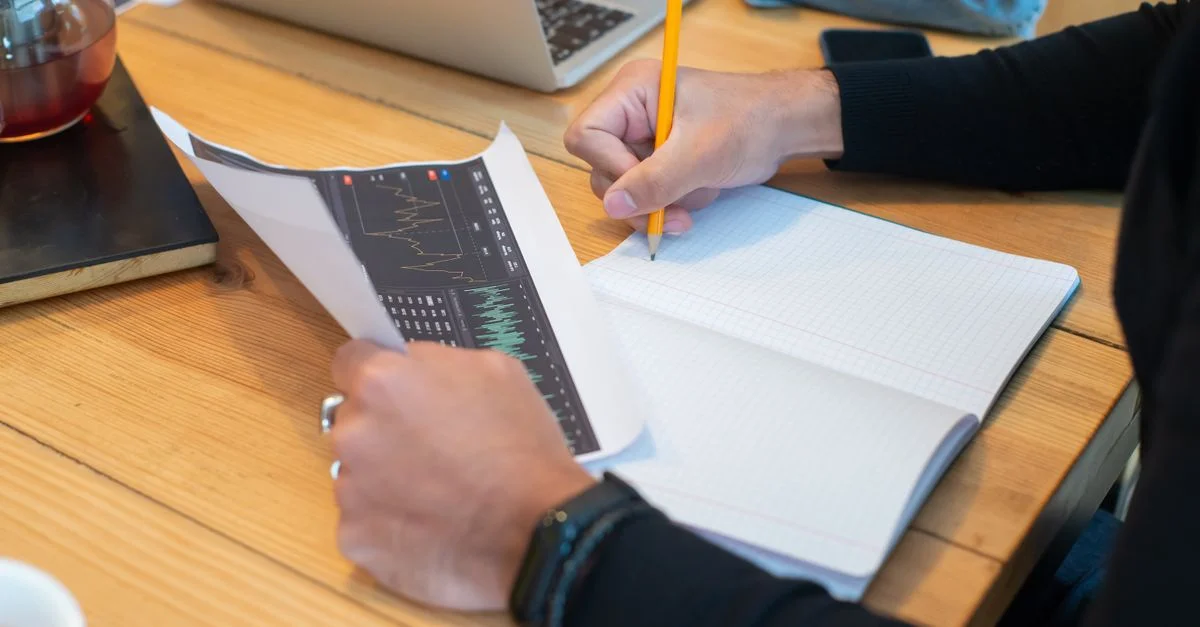 Gros plan sur des mains écrivant des notes dans un cahier lors d'une réunion d'affaires avec un ordinateur portable et des graphiques.