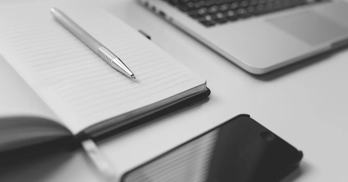 Un espace de travail minimaliste noir et blanc élégant avec un cahier, un ordinateur portable et un smartphone.