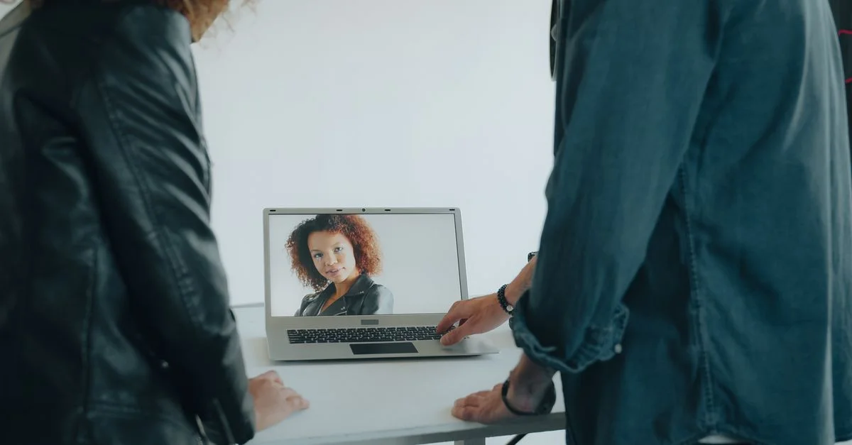 Deux personnes discutent d'un projet, un portrait s'affichant sur l'écran d'un ordinateur portable.