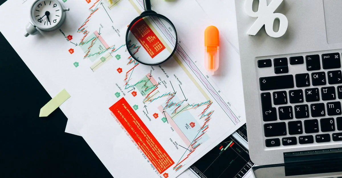 Vue de dessus de documents financiers, graphiques et ordinateur portable organisés sur un bureau.
