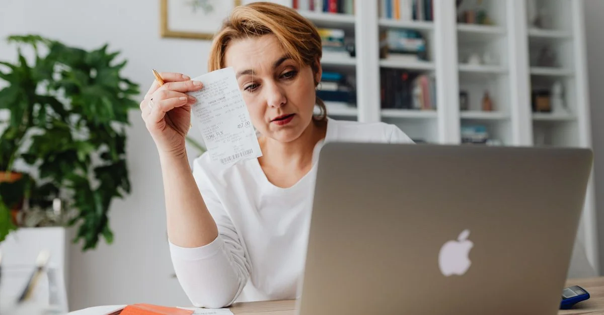 Femme concentrée sur des reçus tout en utilisant un ordinateur portable, reflétant un stress financier.