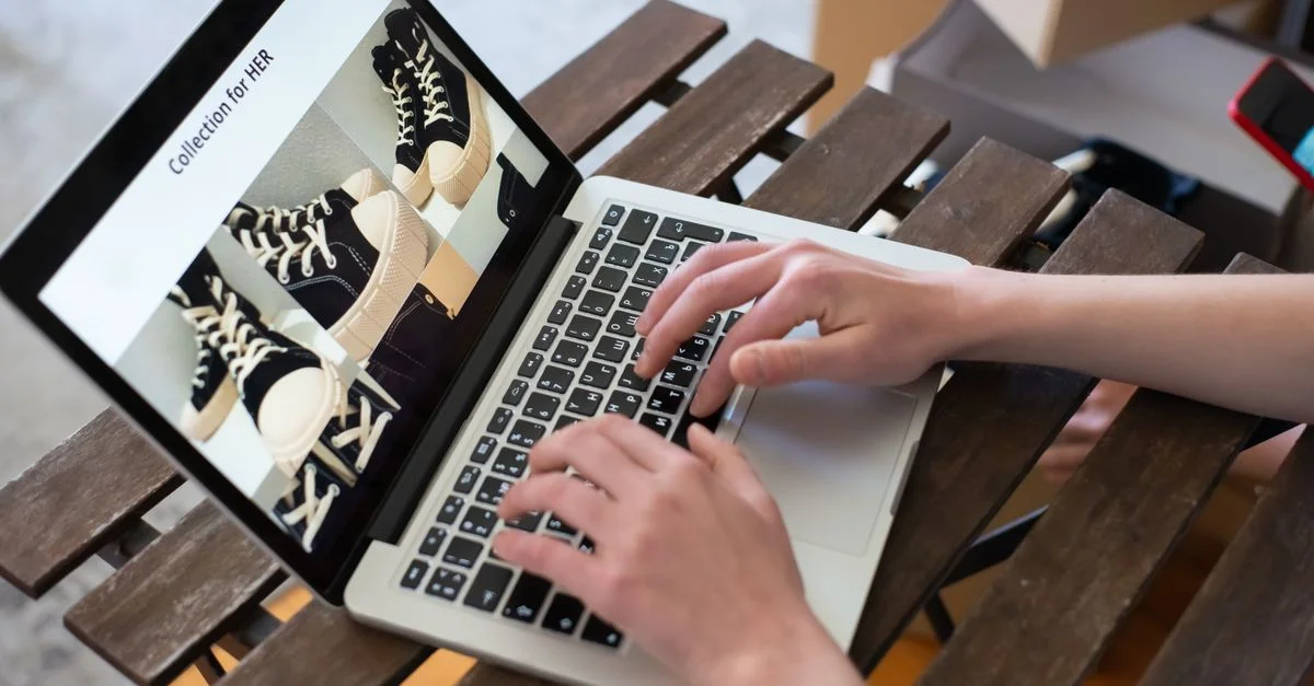 Mains d'une personne parcourant une Collection pour ELLE sur un site de chaussures en ligne avec un ordinateur portable.