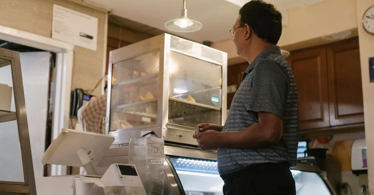 Un homme adulte se tient devant un comptoir de boulangerie à l'intérieur, prêt à acheter de la nourriture.